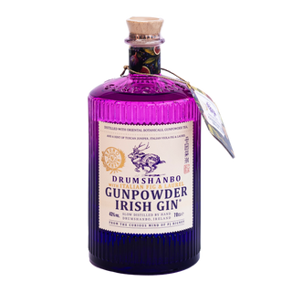 A bottle of Drumshanbo Gunpowder Irish Gin with Italian Fig & Laurel, with a purple glass body, cork stopper, and cream-colored label, shown on a plain white background.