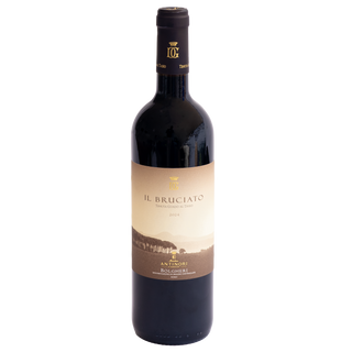 A bottle of Il Bruciato red wine by Antinori Bolgheri, featuring a dark glass bottle with a beige and brown landscape label and a black foil neck seal.